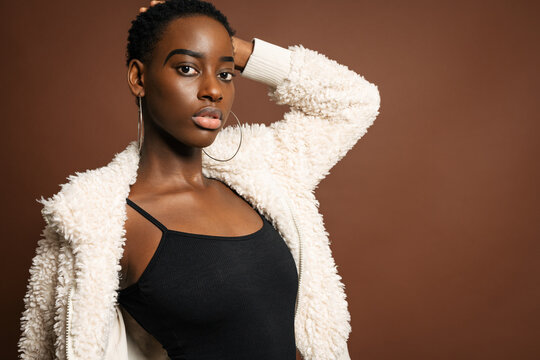 Slender black woman with short hair standing against brown background looking at camera