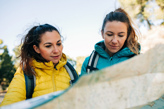 Traveling women standing near car on road with paper map and orientating while looking for direction during vacation