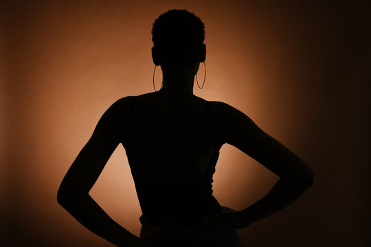 Silhouette of unrecognizable slender female with hands on wait against brown background