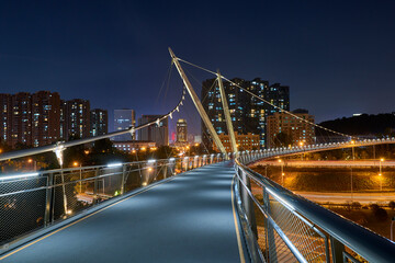 Contemporary suspension pedestrian bridge in creative design crossing road in modern urban city at night
