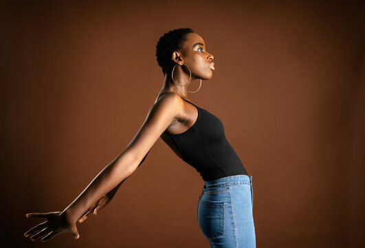 Side view of slender black woman with short hair bending back against brown background