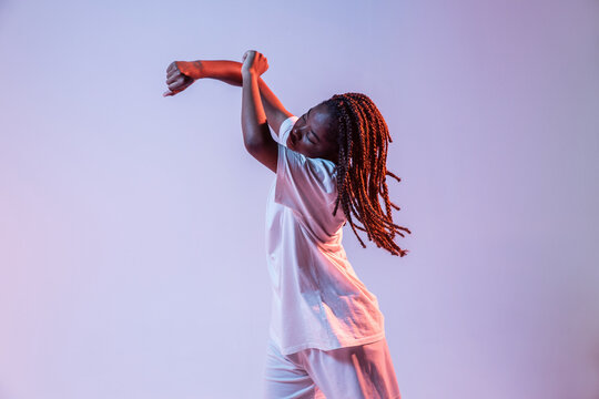 Full body of concentrated African American teen dancing in studio with bright neon light