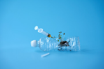  A used plastic bottle containing a fragment of soil with sprouts. A syringe will be inserted into...