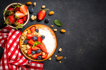 Yogurt granola with fresh berries on black stone table. Top view with copy space. Healthy food, snack or breakfast.