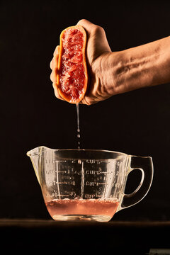 Unrecognizable crop person squeezing ripe grapefruit juice in glass measuring jug placed on table on black background
