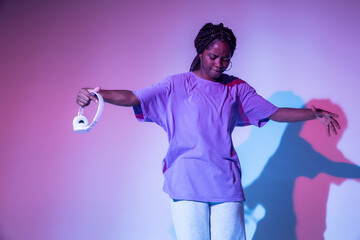 Full body of African American teen girl with headphones in hand performing urban dance movement in bright studio