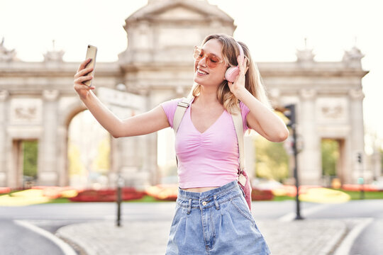 Cheerful teenage female in casual outfit and sunglasses taking self portrait while listening to music on Madrid street