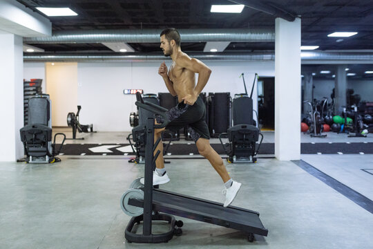 Side view full body of strong enduring man training on sports equipment in spacious gym