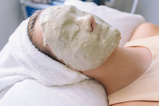 Alginate mask on face of anonymous young female customer lying on couch with closed eyes