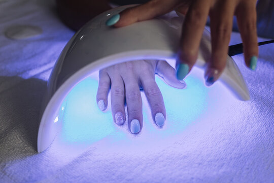 From above of crop anonymous female drying gel nail polish under UV LED lamp in beauty studio