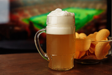 One glass of cold beer and chips, football match in background.