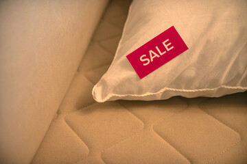 A sticker with the words sale on a white pillow lying on the sofa. Sale of bedroom furniture.