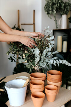 Copped unrecognizable female horticulturist creating bouquet on table with assorted tools at home