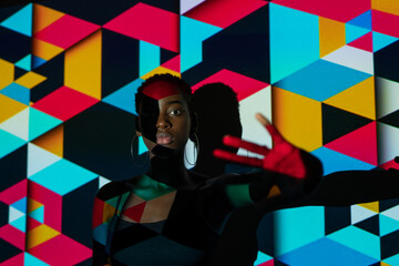 African American female model looking at camera and gesturing stop while standing under colorful geometric projection