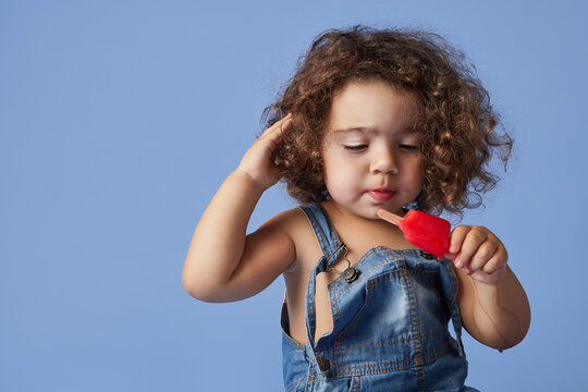 Upset little girl standing with ice cream against studio blue background