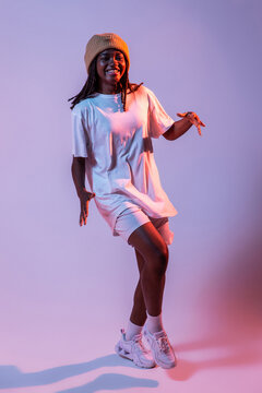 Full body of concentrated African American teen dancing with hands outstretched in studio with bright neon light
