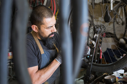 Serious adult man in apron and gloves repairing wheel of bike in modern garage