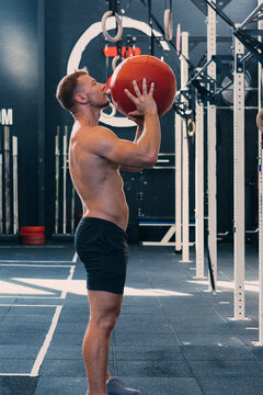 Side view of sportsman with naked torso throwing medicine ball during functional workout in gym