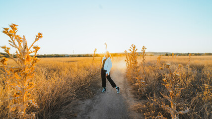 Side view of active young lady in trendy outfit dancing in dry fiends against cloudless blue sky in countryside