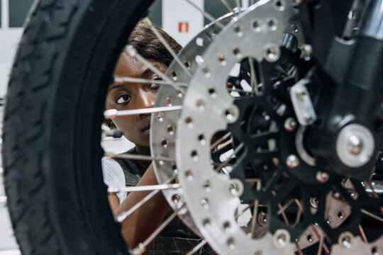 Skilled African American female mechanic fixing wheel of custom motorcycle while working in professional workshop