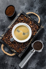 Coffee cup and beans in old wooden tray. Black background. Top view