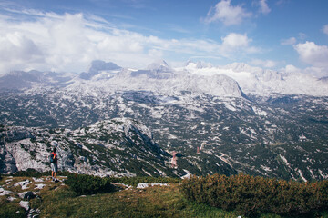exemplary difference between a small person and a vast area of nature. The backpacker with a red T-shirt climbed the Krippenstein mountain and looks around and enjoys the view