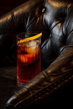 Shiny glass of fresh Negroni cocktail with orange slice garnished with slice of orange peel on leather armchair