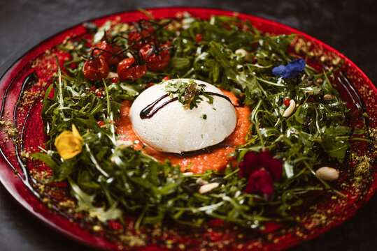 Yummy burrata cheese on cold tomato cream with arugula leaves and cherry tomatoes with truffles and peanuts
