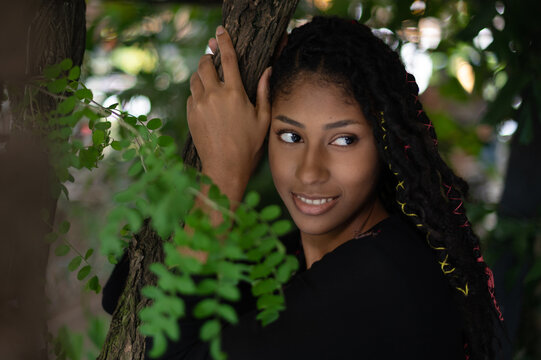 Portrait of attractive afro latina woman with dreadlocks hugging a tree