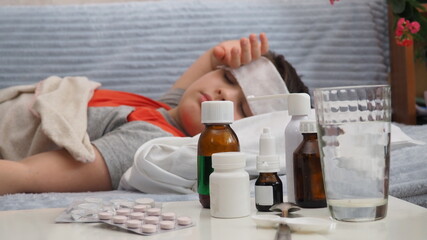sick kid with runny nose and fever heat lying on couch at home, mom treats son, gives medicine, drinks pills, blows his nose.