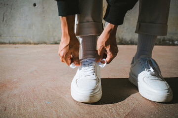 From above of crop unrecognizable trendy guy tying laces of stylish sneakers while standing on street on sunny day