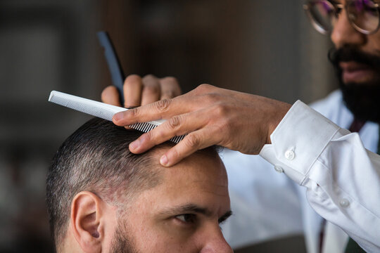 Crop stylish ethnic male beauty master removing hair of masculine client using straight razor in hairdressing salon
