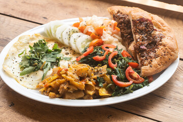 Jajka smażone z warzywami i pizzą, pyszne śniadanie na białym talerzu na drewnianym stole.