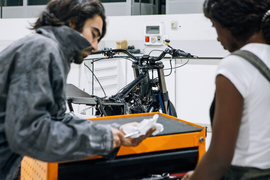 Male mechanic with paper list in hands and African American female coworker choosing necessary tools while working together in modern repair service center