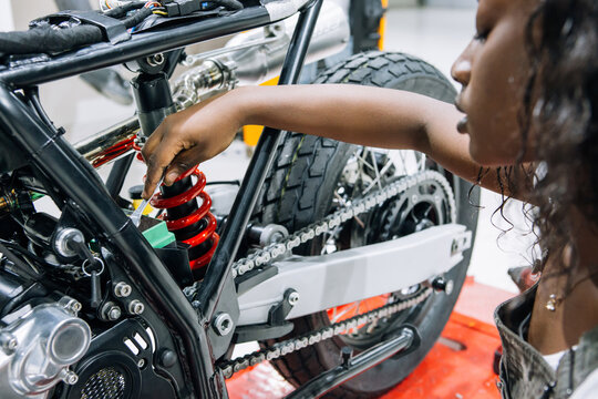 Side view of African American female mechanic with wrench fixing custom motorbike while working in workshop