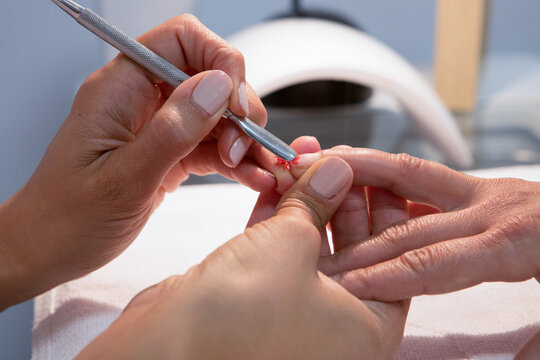 Crop unrecognizable female beauty master applying red varnish on nail of woman during manicure procedure in spa center