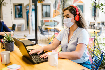 latin woman wearing face mask in coworking creative space working with computer during corona virus pandemic in Latin America