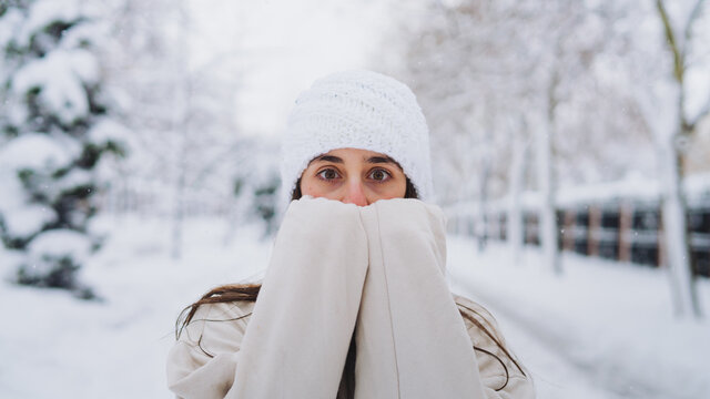 Anonymous young amazed female in knitted hat covering face while looking at camera on pathway between trees in Spain