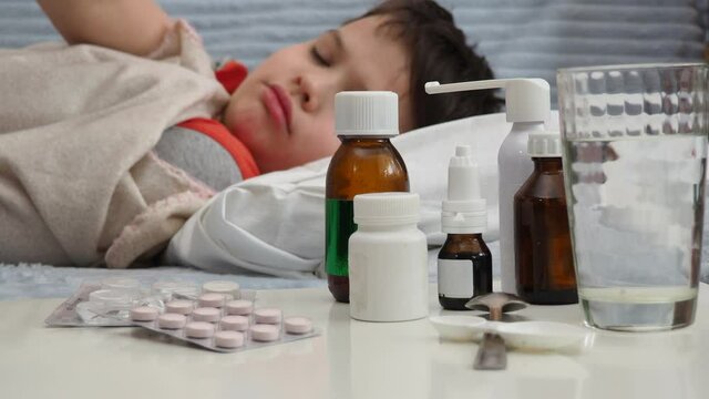 sick kid with runny nose and fever heat lying on couch at home, mom treats son, gives medicine, drinks pills, blows his nose.