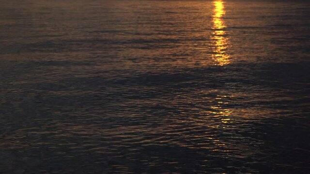 4k video of beautiful smooth golden dark sunrise or sunset sea waves with magic sun light reflections on surface of water. Abstract natural background
