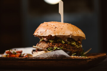 Low angle of yummy burger with vegetarian patty and grilled shiitakes between buns near sweet potato and carrot slices with alioli sauce on dark background