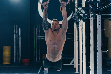 Low angle of concentrated athletic male with naked torso doing abs exercises on gymnastic rings during functional training in gym