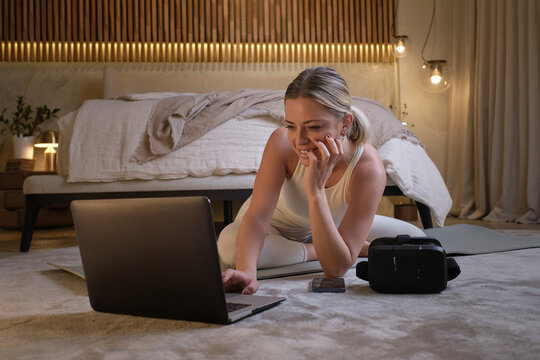 High angle of female sitting on mat and choosing online tutorial on laptop while preparing for doing yoga at home - Powered by Adobe