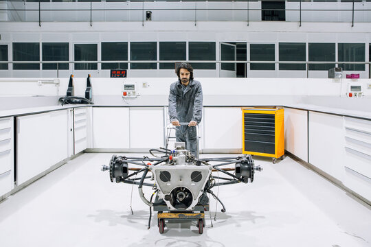 Male technician transporting disassembled motorbike on trolley while working in modern repair service workshop
