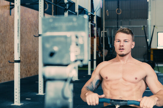 Focused male athlete with strong naked torso sitting on rowing machine and doing exercises during functional workout