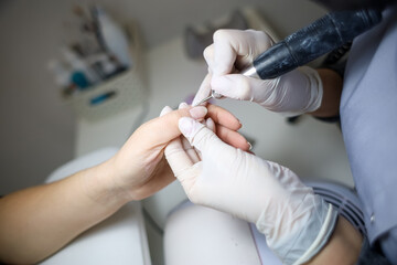 manicure master holds the client's fingers, processing them with a manicure machine