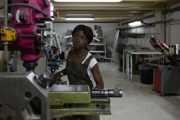 Professional young African American female mechanic processing detail on lathe machine while working in repair workshop