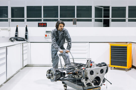 Male technician transporting disassembled motorbike on trolley while working in modern repair service workshop