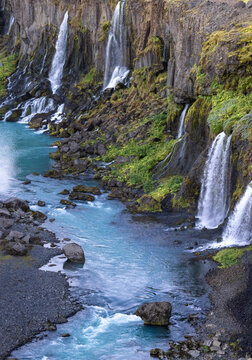 Spectacular view of rapid cascades flowing from rough rocky cliff covered with lush greenery into tranquil blue reservoir in peaceful nature