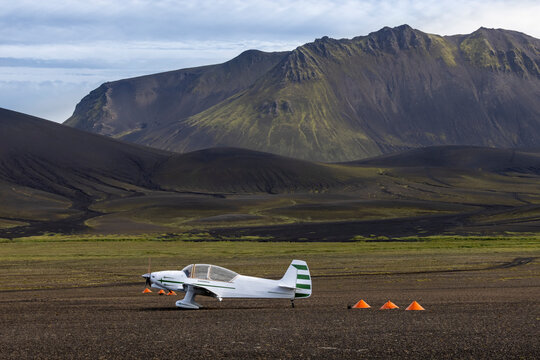 White monoplane parked on spacious grassy valley surrounded by rough picturesque mountain range in Nordic nature